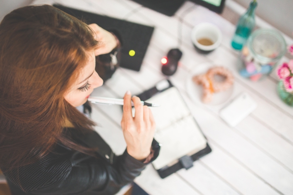 Woman holding a pen and smiling thoughtfully at a desk with a notebook, tea and flowers, illustrating content planning