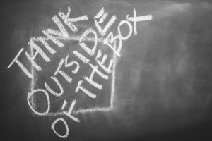 Think outside the box written in chalk on a blackboard in scattered directions