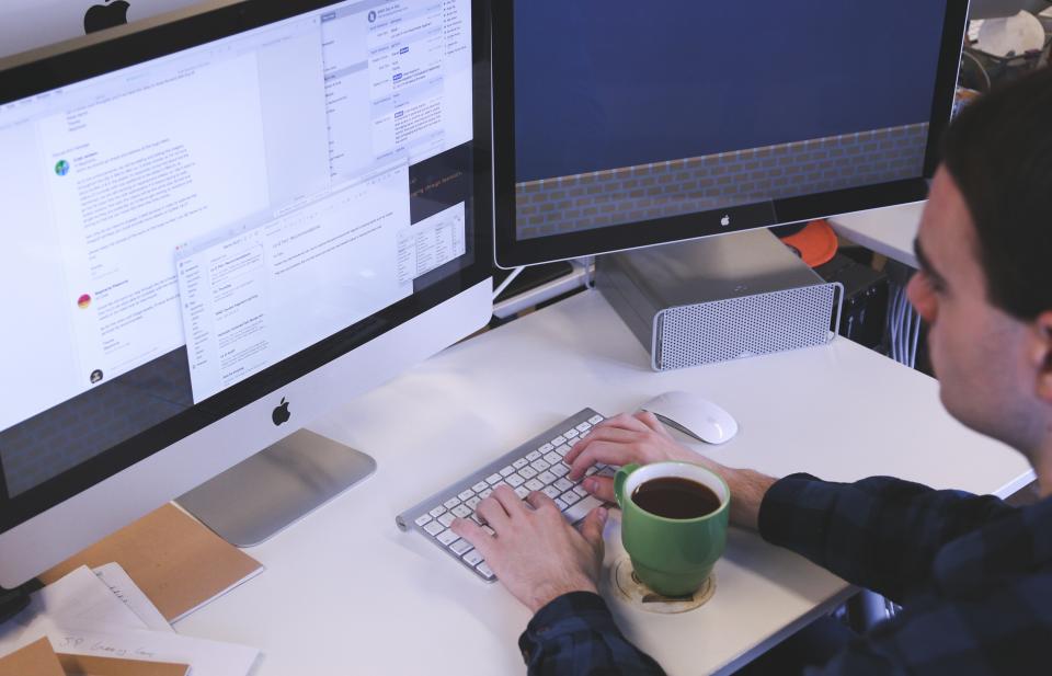 Man working at dual Apple iMac setup with coffee mug, managing G Suite apps and storage