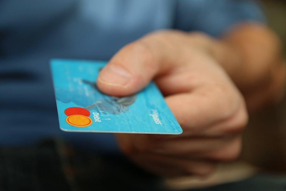Hand holding a blue Mastercard debit card toward the camera, representing online payment for ecommerce