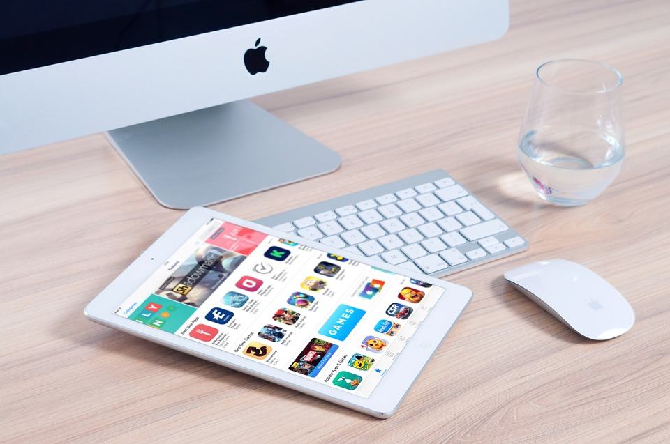 iPad showing the App Store next to an iMac, keyboard and Magic Mouse on a wooden desk