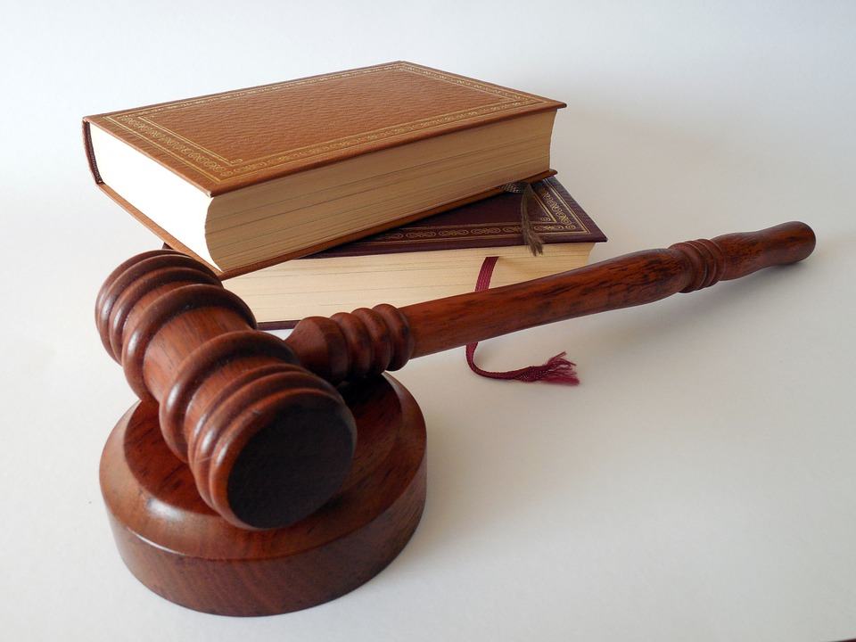 Wooden judge's gavel resting on its block beside two stacked law books with red ribbon bookmarks