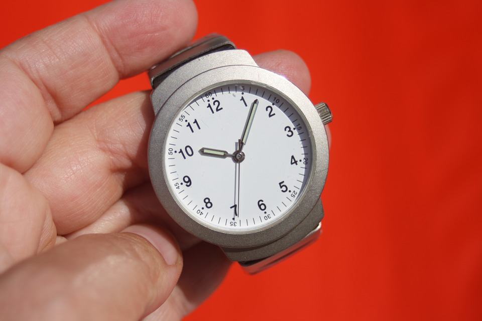 Hand holding a silver wristwatch against a red background, representing the importance of website speed and time
