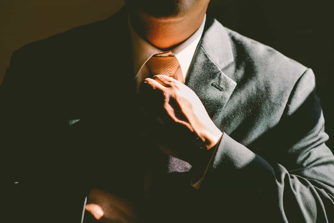 Close-up of a businessman in a dark suit adjusting his tie, representing professional brand identity