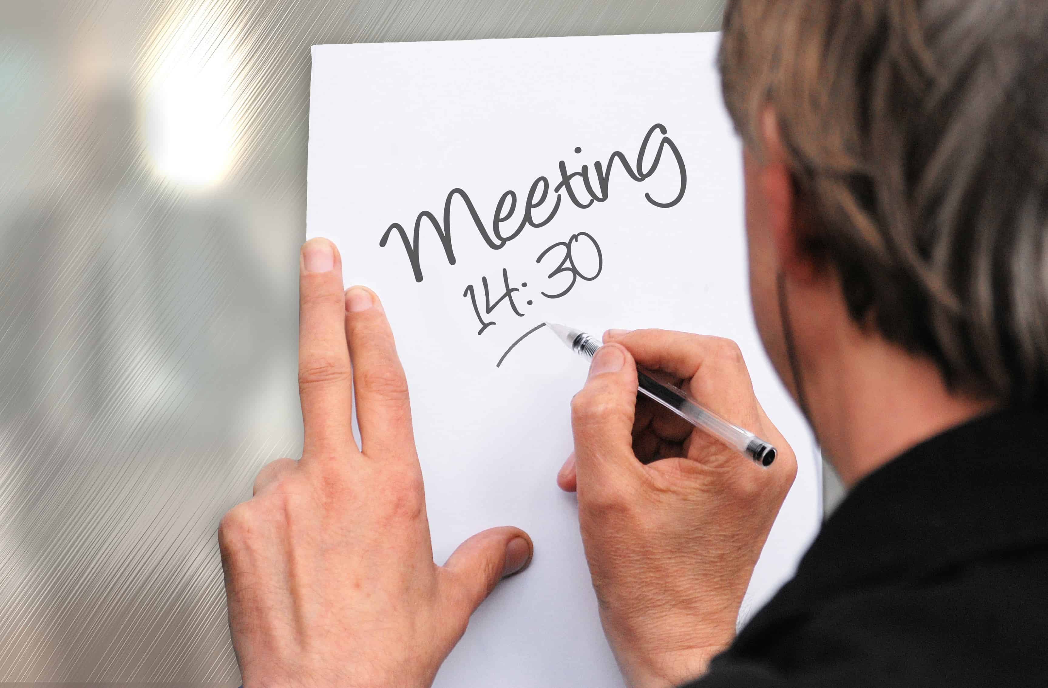 Person writing Meeting 14:30 on a piece of paper, illustrating time management scheduling