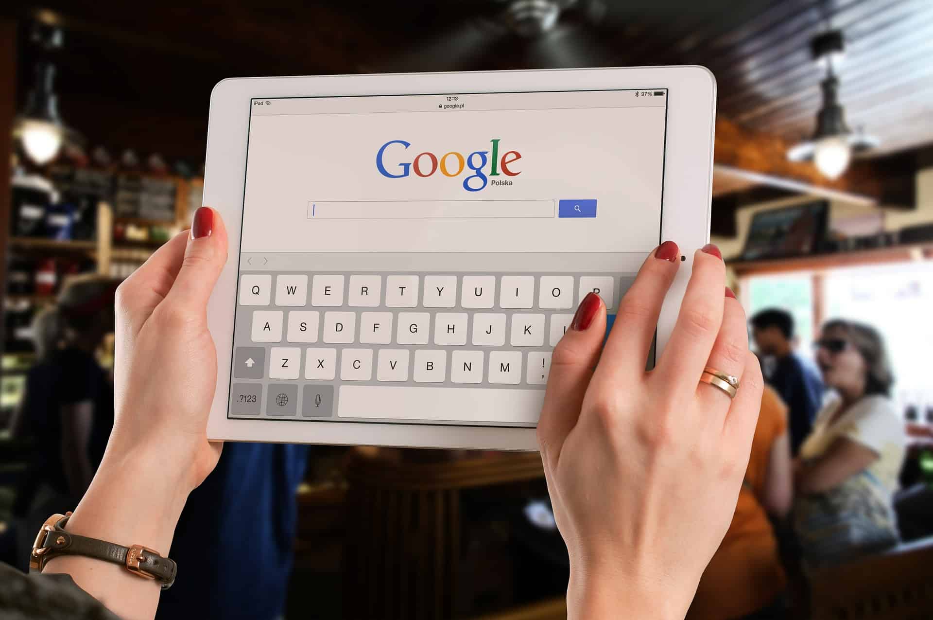 Woman holding an iPad displaying the Google search homepage with an on-screen keyboard in a cafe
