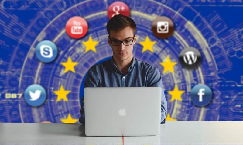 Man at a laptop with the EU flag and social media icons including Facebook, Twitter and YouTube in the background