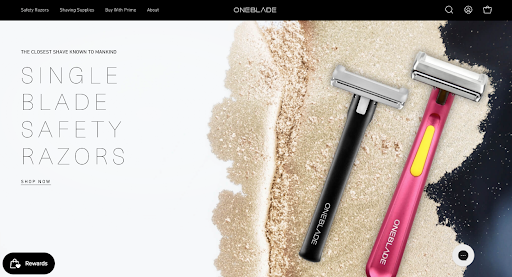 OneBlade single blade safety razor website homepage showing black and pink razors on a sandy background
